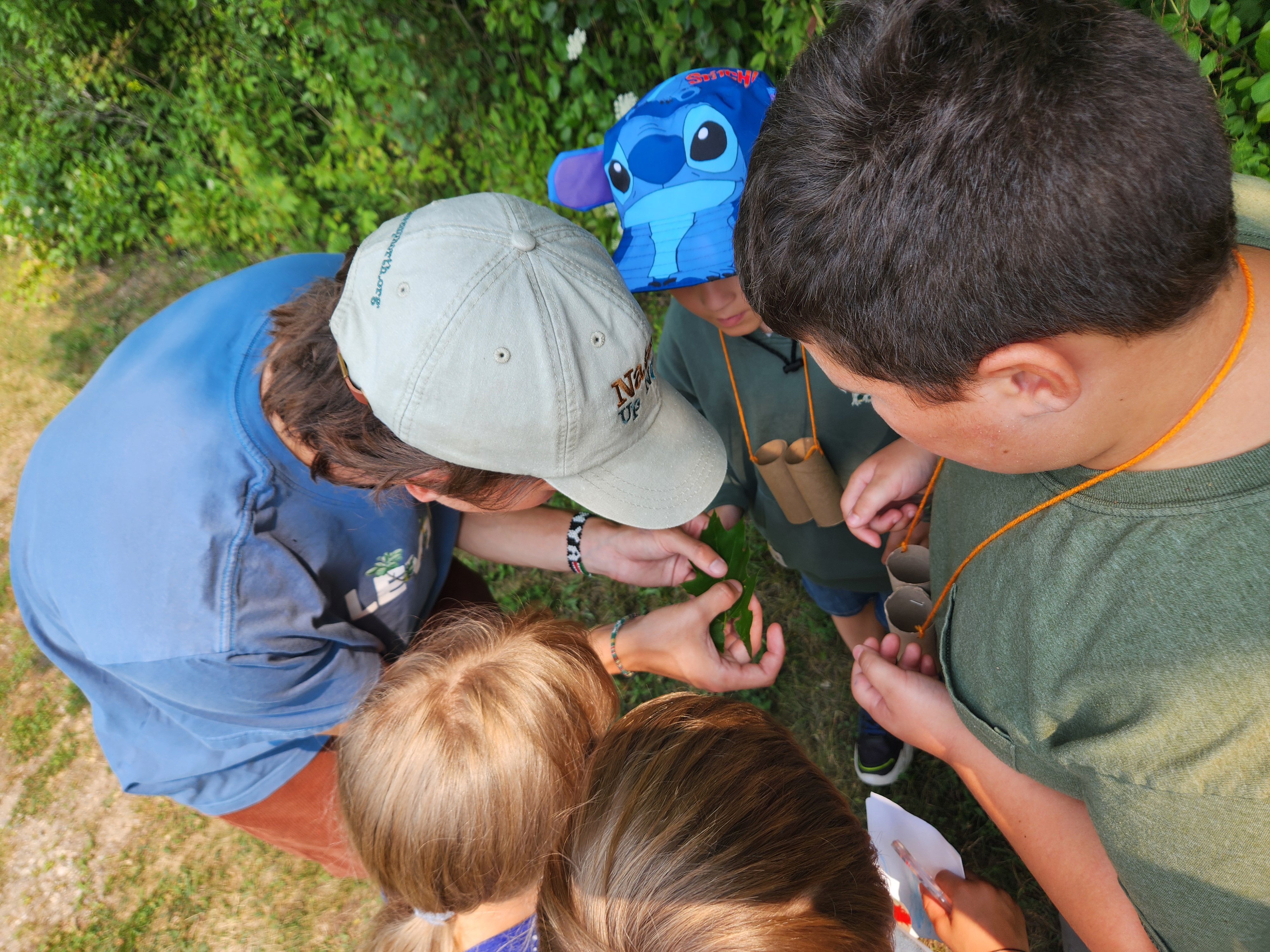 Summer Naturalist Will shows a leaf to elementary students.