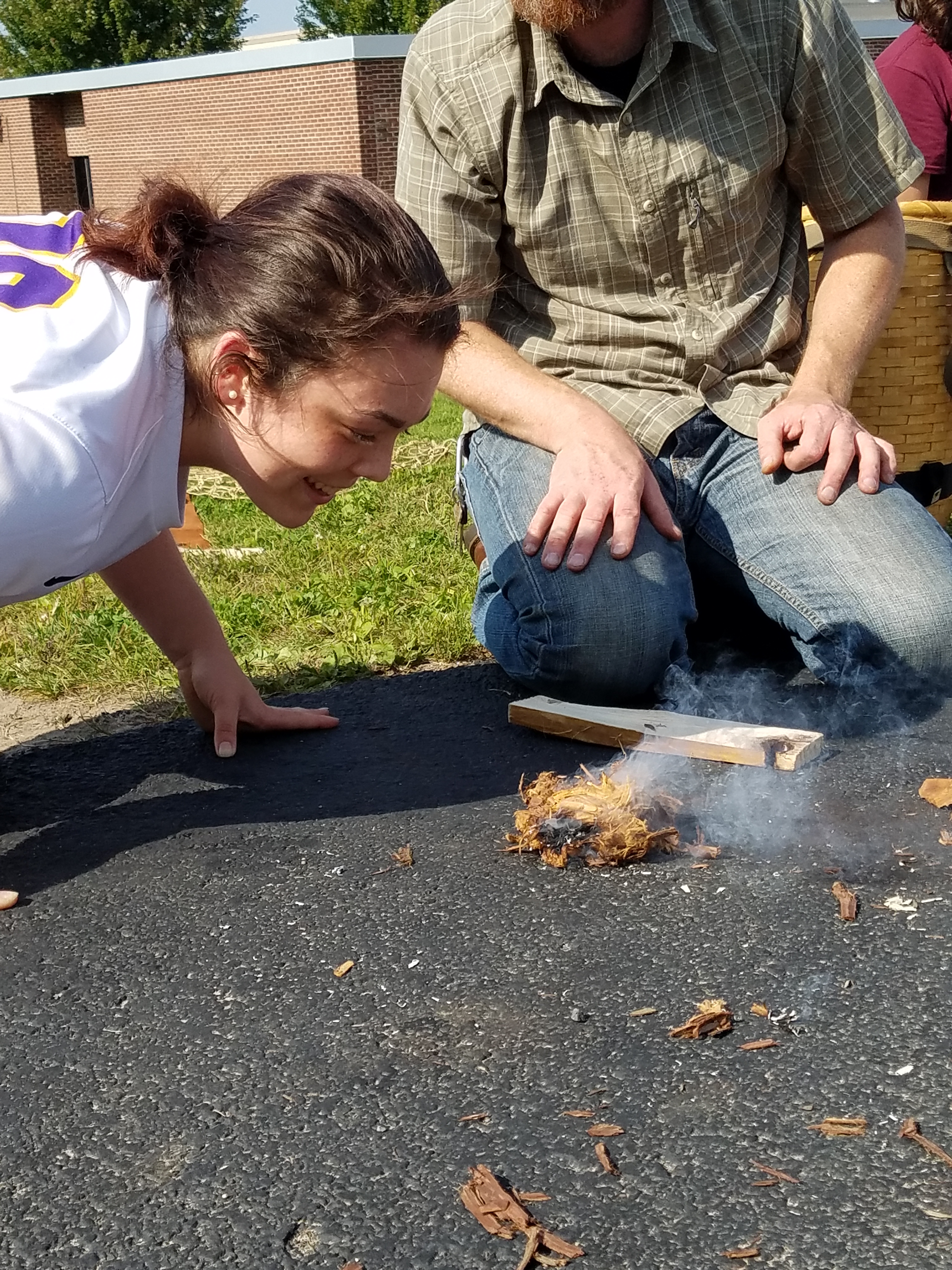 Here the student gently blows on the embers she created to feed the flame.