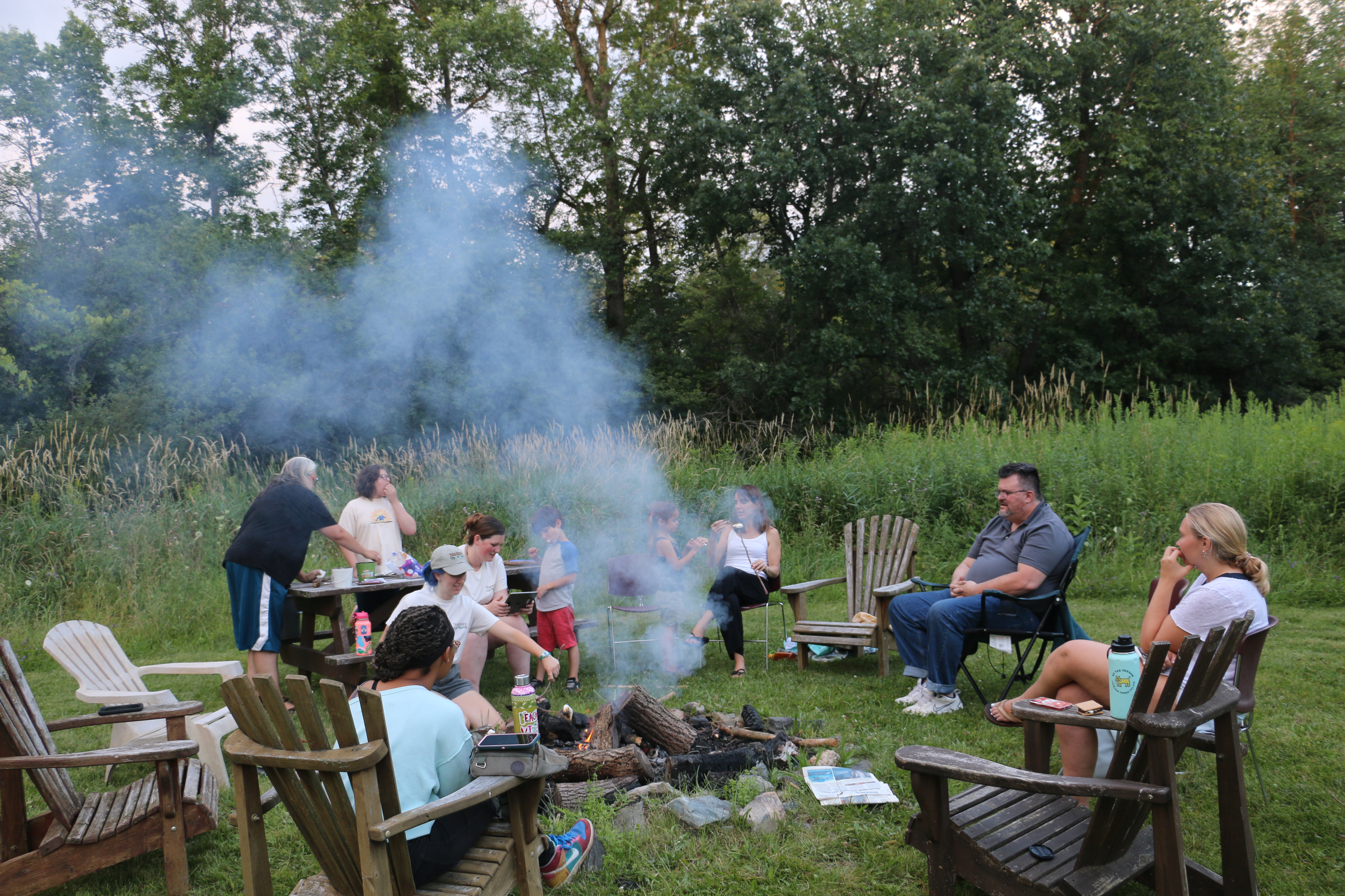 A group of people sitting around a campfire, smoke blowing up