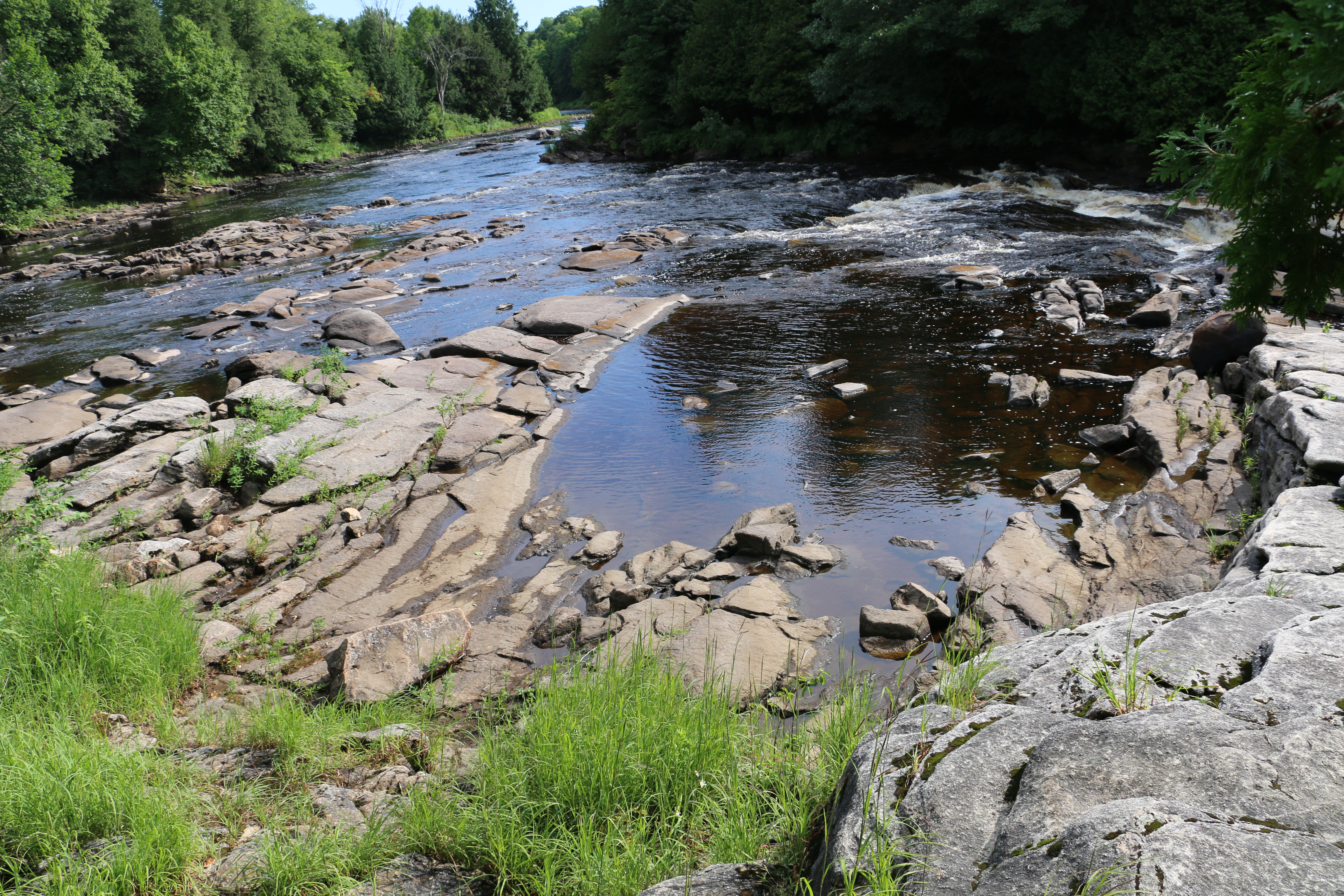 A wide shot of a river dotted with rock formations, flanked by trees in the background