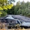 Waterfall half hidden by rock formations that have circular potholes carved into them by water over time. 