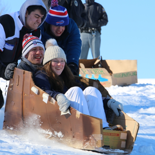 College students pushing cardboard sled down hill