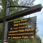 Lampson falls trailhead sign is brown with yellow lettering that says Grasse River wild forest forest preserve lampson falls parcel NYS department of environmental conservation lampson falls and points towards the trail