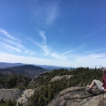 A hiker sits to the right on rocks on Ampersand Mountain in New York State's Adirondacks.