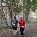 A person in red and a person in gray walk down a wooded trail